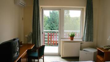 Ein Hotelzimmer mit Bett, Schreibtisch mit Fernseher, Stuhl, Heizkörper und Fenster mit Blick auf Bäume und einen Zaun.