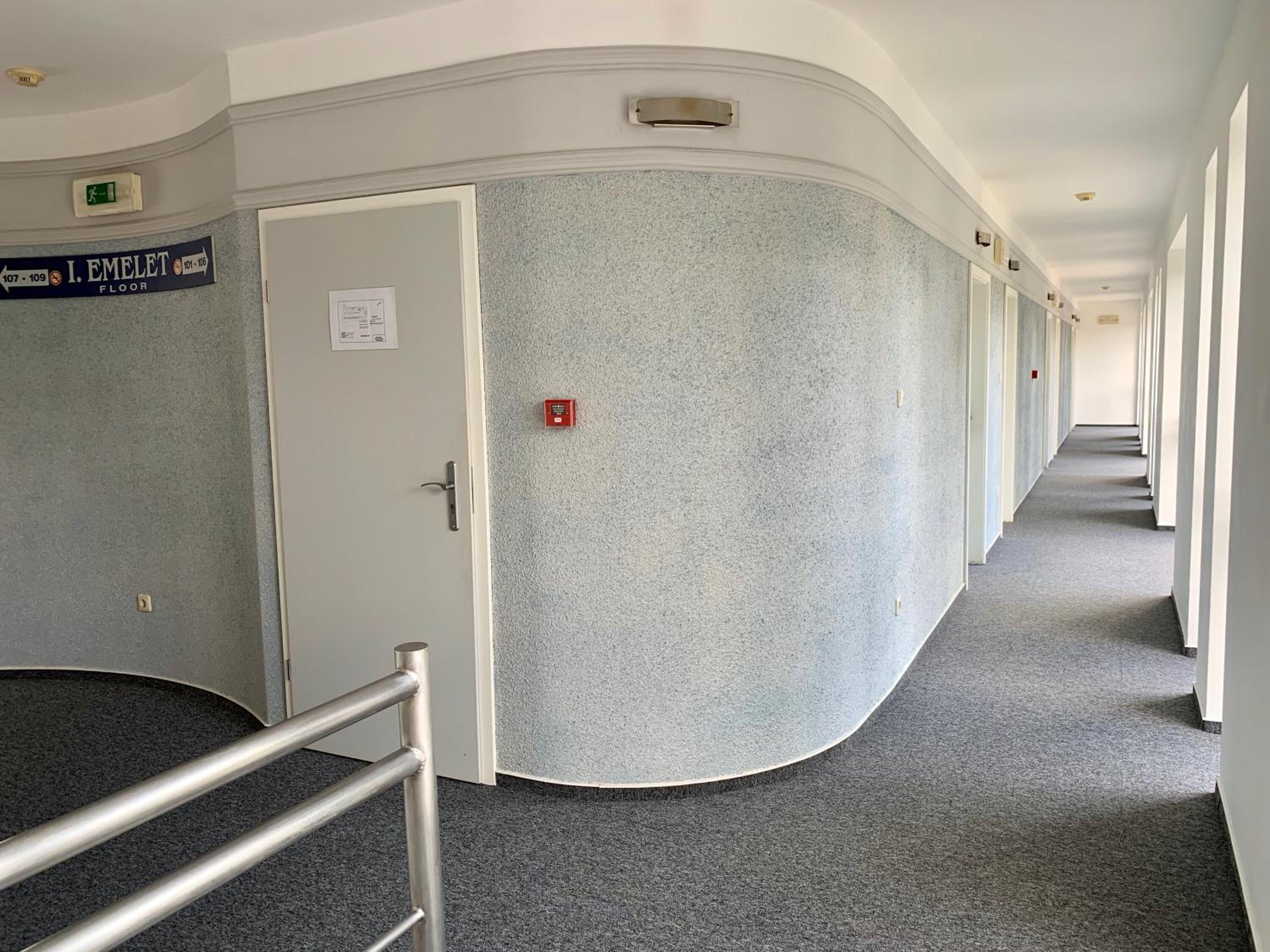 Ein Hotelgang mit einem Schild, das die Etage angibt, einem Rauchmelder und einer Handlauf.