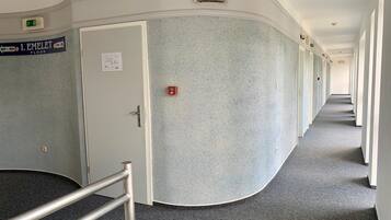 Ein Hotelgang mit einem Schild, das die Etage angibt, einem Rauchmelder und einer Handlauf.