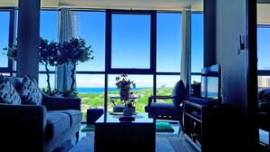 Ein Wohnzimmer mit großem Fenster, einer Couch, einem Couchtisch und einem Fernseher.