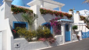 Un edificio blanco con puertas y ventanas azules, rodeado de flores y plantas coloridas.