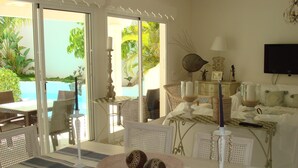 Una habitación con vista a una piscina, un comedor con mobiliario de mimbre y una cama con mantel individual a cuadros.