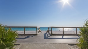 A wooden boardwalk leading to a beach with clear blue water and a sunny sky.