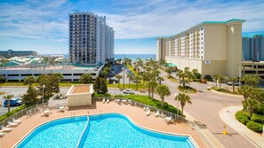 A hotel with a swimming pool, palm trees, and a view of the ocean.