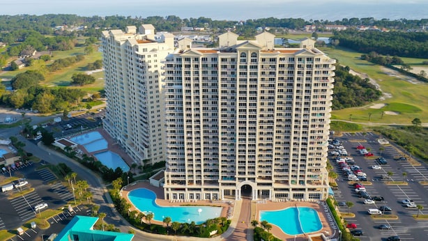 Un grand hôtel avec de nombreux balcons, une piscine et, au loin, un terrain de golf.