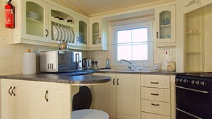 A kitchen with white cabinets, a microwave, a stove, and a window. - A comfortable Cornish countryside retreat in Coosewartha (Truro)