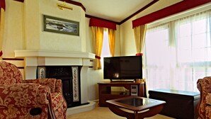 A living room with a fireplace, a television on a stand, and two patterned armchairs. - A comfortable Cornish countryside retreat in Coosewartha (Truro)