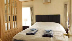 A bedroom with a bed, a wooden wardrobe with glass doors, a nightstand, and a window with curtains. - A comfortable Cornish countryside retreat in Coosewartha (Truro)