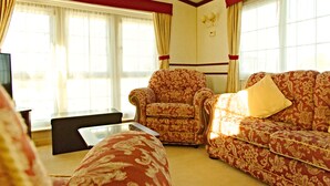 A living room with a patterned sofa, armchair, and ottoman, a coffee table, and a television. - A comfortable Cornish countryside retreat in Coosewartha (Truro)