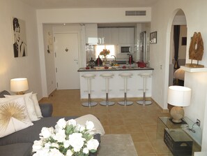 A modern kitchen with white cabinets, a central island with bar stools, and a dining area with a sofa and a coffee table.