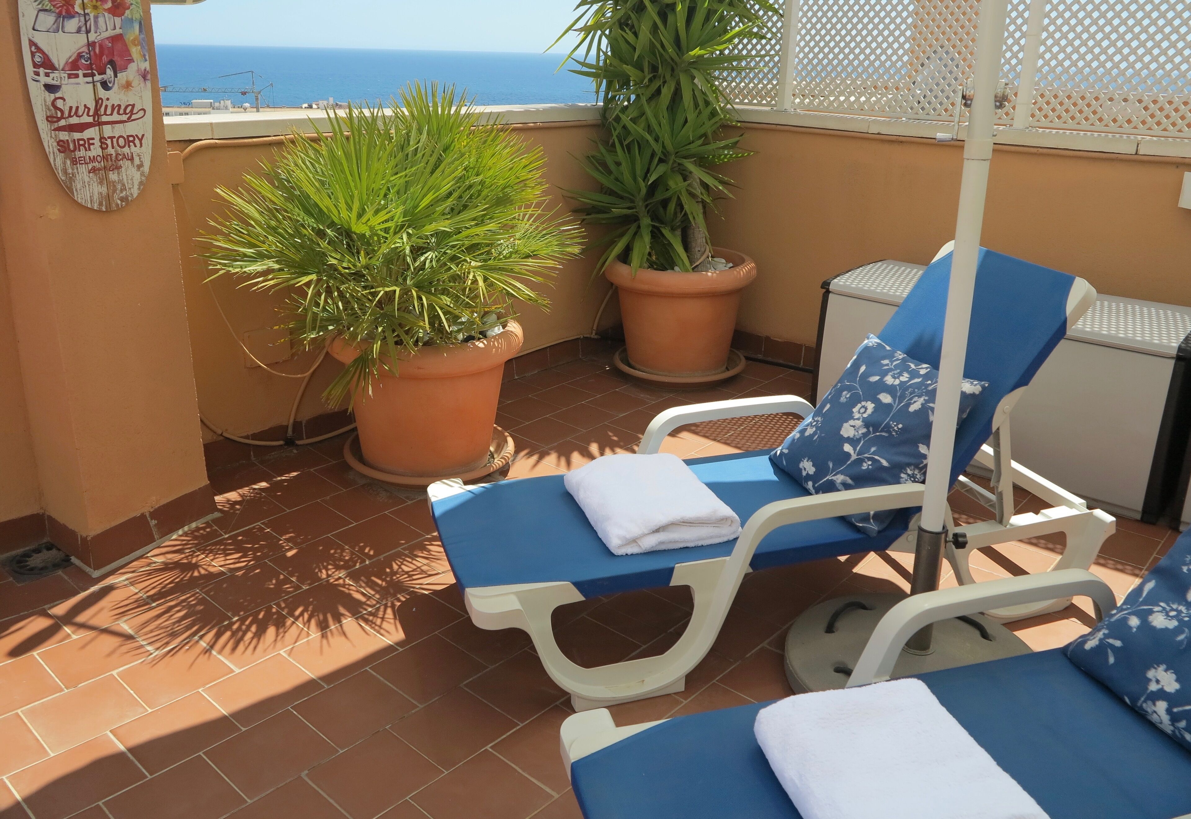 A balcony with two sun loungers, potted plants, and a view of the sea.