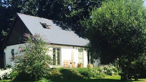 A white house with a dark roof, surrounded by a well-maintained lawn and flowering bushes. - Hillcrest Barn (Kilgetty)