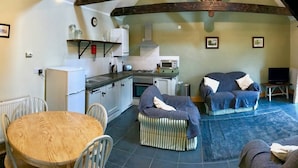 A cozy living room with a dining table, two sofas, and a kitchen area with a stove and microwave. - Hillcrest Barn (Kilgetty)