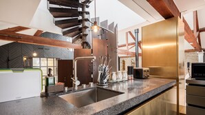 A modern kitchen with a granite countertop, stainless steel appliances, and a unique spiral staircase. - Skyline Water Front Penthouse Apartment (London)