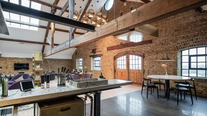 A spacious kitchen with a large island, exposed brick walls, and a high ceiling with wooden beams. - Skyline Water Front Penthouse Apartment (London)