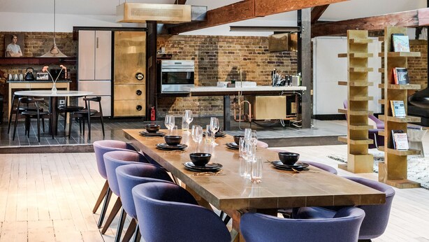 Un amplio comedor con una larga mesa de madera y sillas modernas, una pared de ladrillo y un tragaluz.