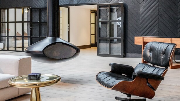 A spacious interior with a high ceiling, exposed wooden beams, a large black chimney, and a modern seating area with a leather chair and a glass table. - Skyline Water Front Penthouse Apartment (London)