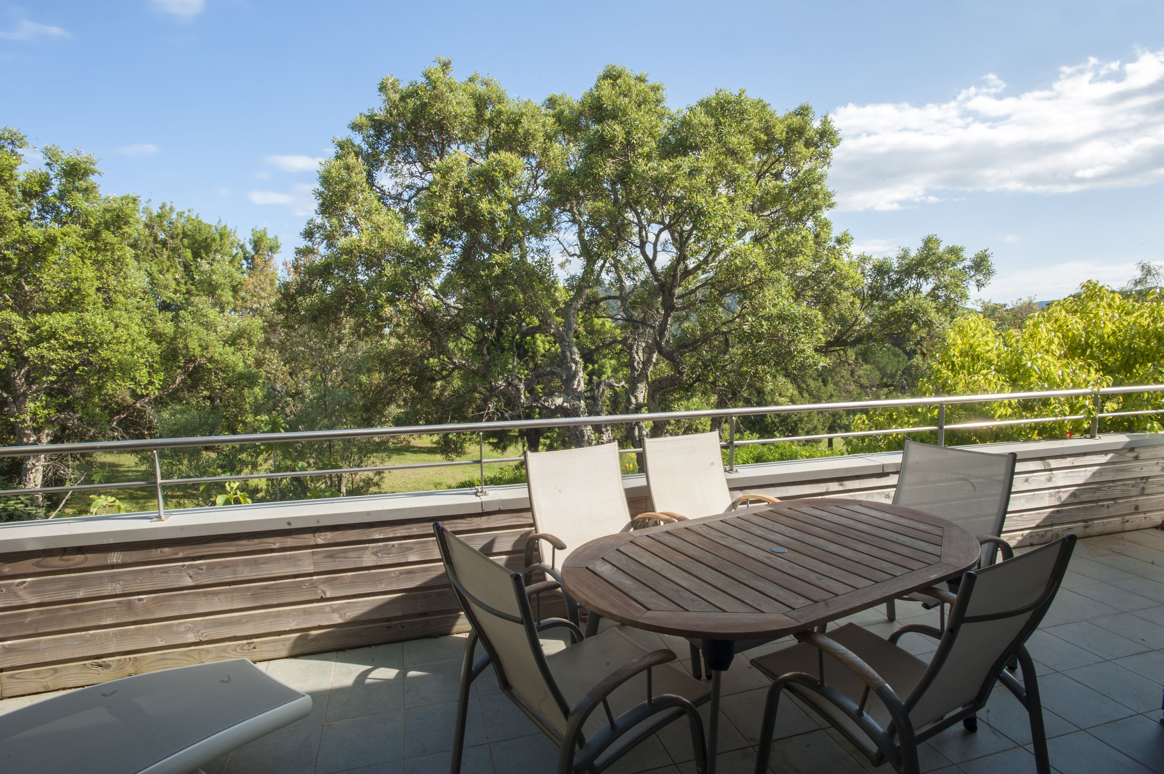 An outdoor patio with a wooden table and chairs, surrounded by a metal railing.