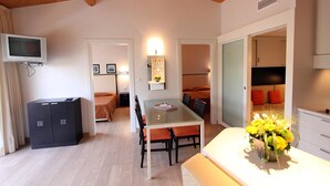 Een knus leefgedeelte met een eettafel, een tv aan de muur, een klein kastje en een bloemenboeket op het aanrecht.