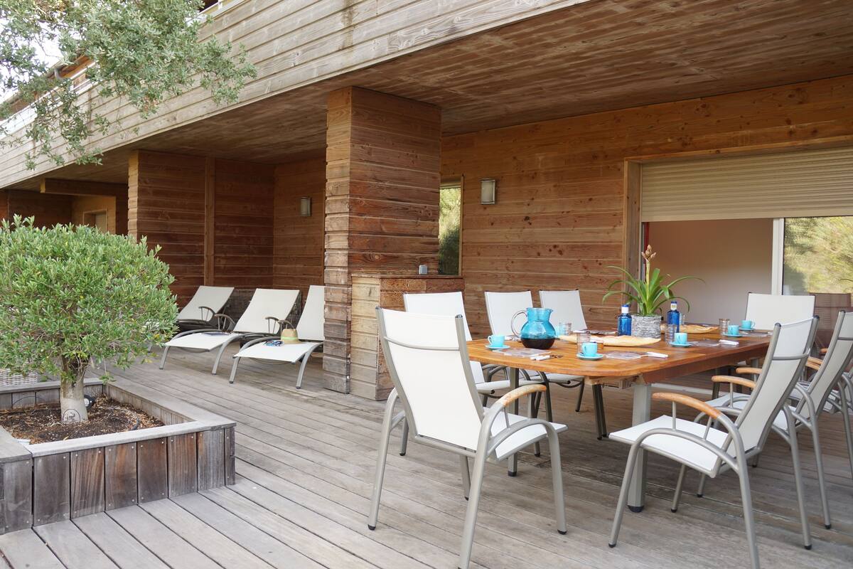 Een houten terras met een eettafel en stoelen, omgeven door een houten omheining en een kleine boom.
