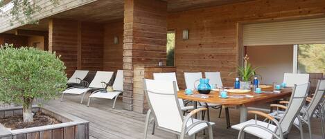Una terraza de madera con una mesa y sillas para comer, rodeada por un cerco de madera y un pequeño árbol.