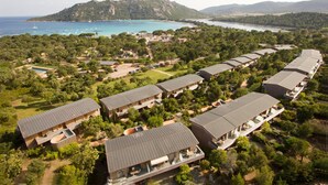 Luchtbeeld van een resort met meerdere gebouwen, een zwembad en een bergachtige achtergrond.