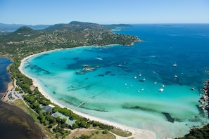 Vista aérea de una zona costera con aguas turquesas cristalinas, una playa de arena y varias embarcaciones fondeadas cerca de la orilla.