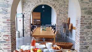 Mesa posta para o pequeno-almoço, com alimentos e vista para uma sala de jantar através de uma porta arqueada.