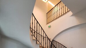 Escadaria curva com guarda-corpo preto e um vaso de planta ao lado.