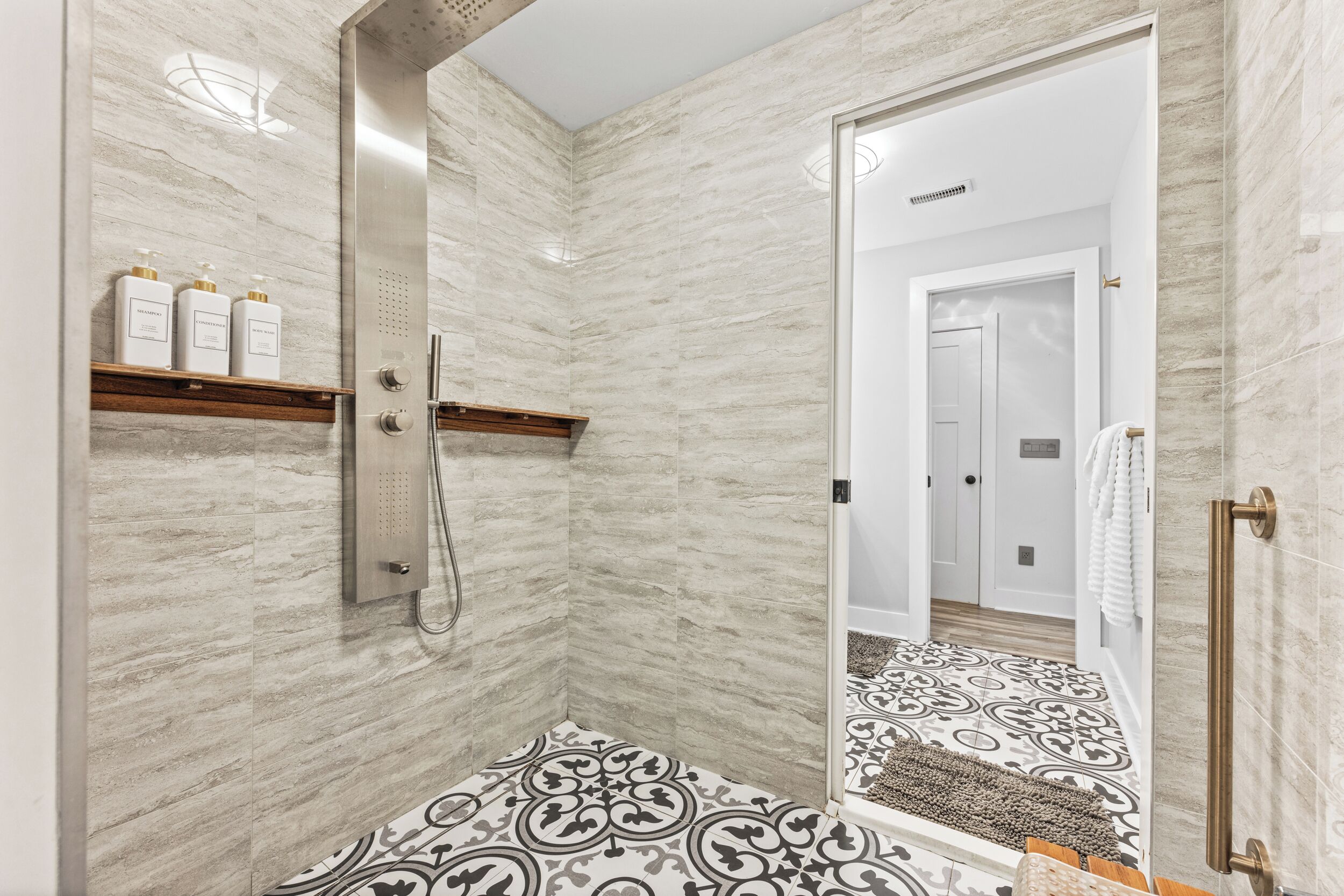 A modern bathroom with a shower, a large mirror, and a patterned floor.
