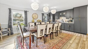 Un coin repas avec une table et des chaises en bois, un tapis à motifs et une grande fenêtre avec des rideaux.