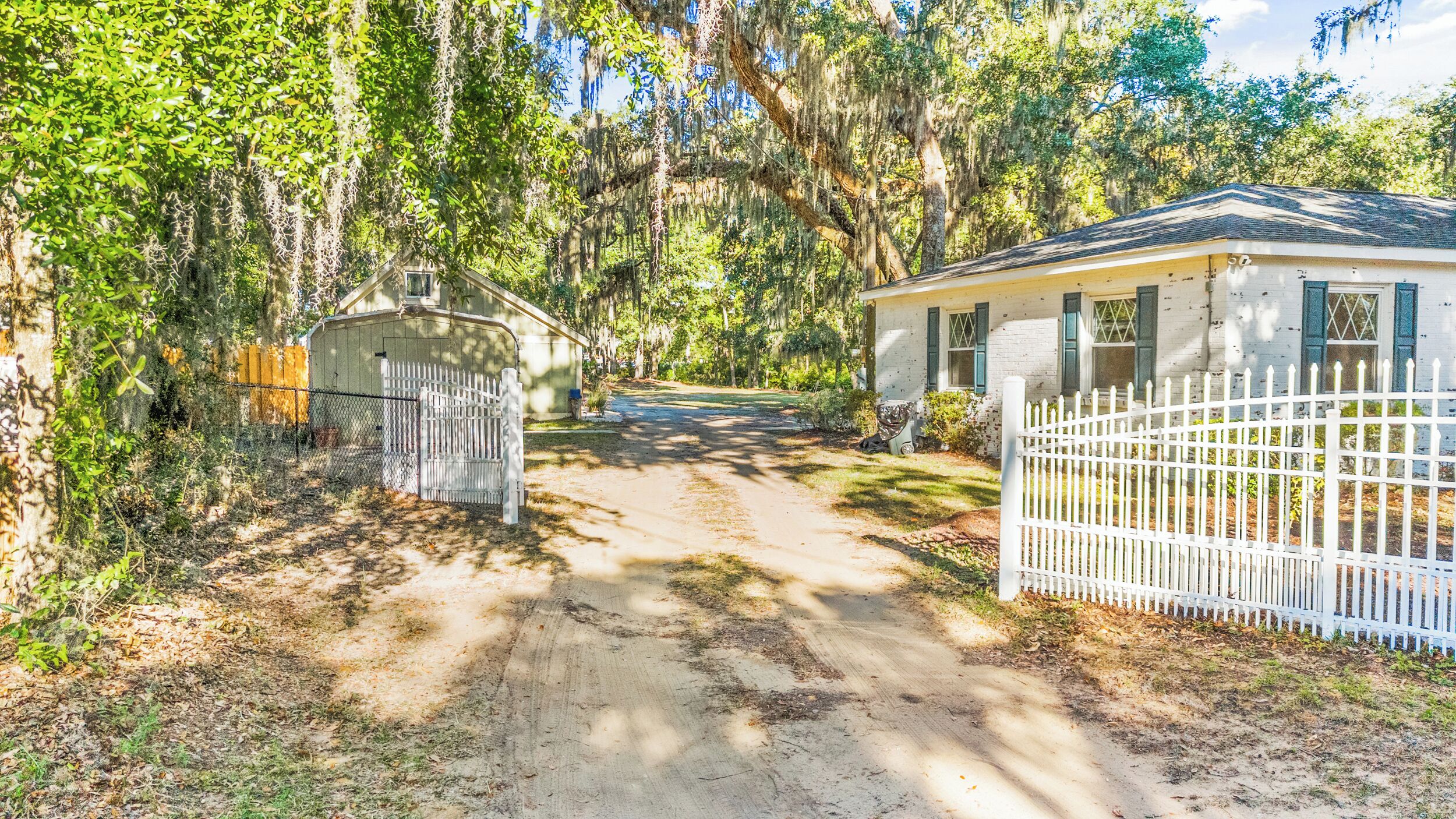 A gated property with a dirt driveway leading to a house with a gabled roof and a garage.