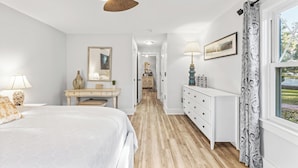 Une chambre à coucher comprenant un lit, un bureau, une commode, un ventilateur de plafond et une fenêtre avec des rideaux.