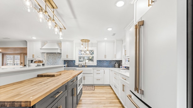 Une cuisine moderne avec des meubles blancs, un plan de travail en bois et un îlot central.