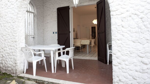 A white textured exterior wall, a white table with four chairs, and a doorway leading to an interior space. - M107 - Marcelli, three-room apartment with garden 200m from the sea (Marcelli)