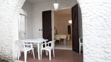 Una parete esterna bianca con texture, un tavolo bianco con quattro sedie e un'apertura che dà accesso a un ambiente interno.