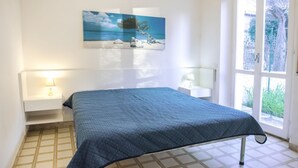 A bedroom with a bed, bedside tables, a painting, and a view through a window. - M107 - Marcelli, three-room apartment with garden 200m from the sea (Marcelli)