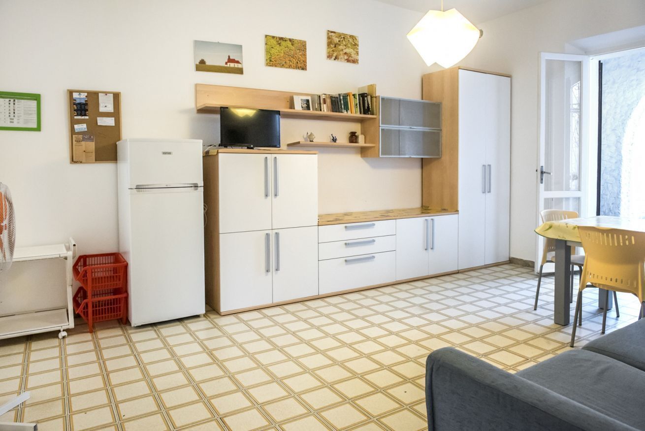 Una cucina compatta con mobili bianchi, un frigorifero, un forno a microonde e un piccolo angolo ristoro con tavolo e sedie.
