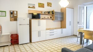 A compact kitchen with white cabinets, a refrigerator, a microwave, and a small dining area with a table and chairs. - M107 - Marcelli, three-room apartment with garden 200m from the sea (Marcelli)