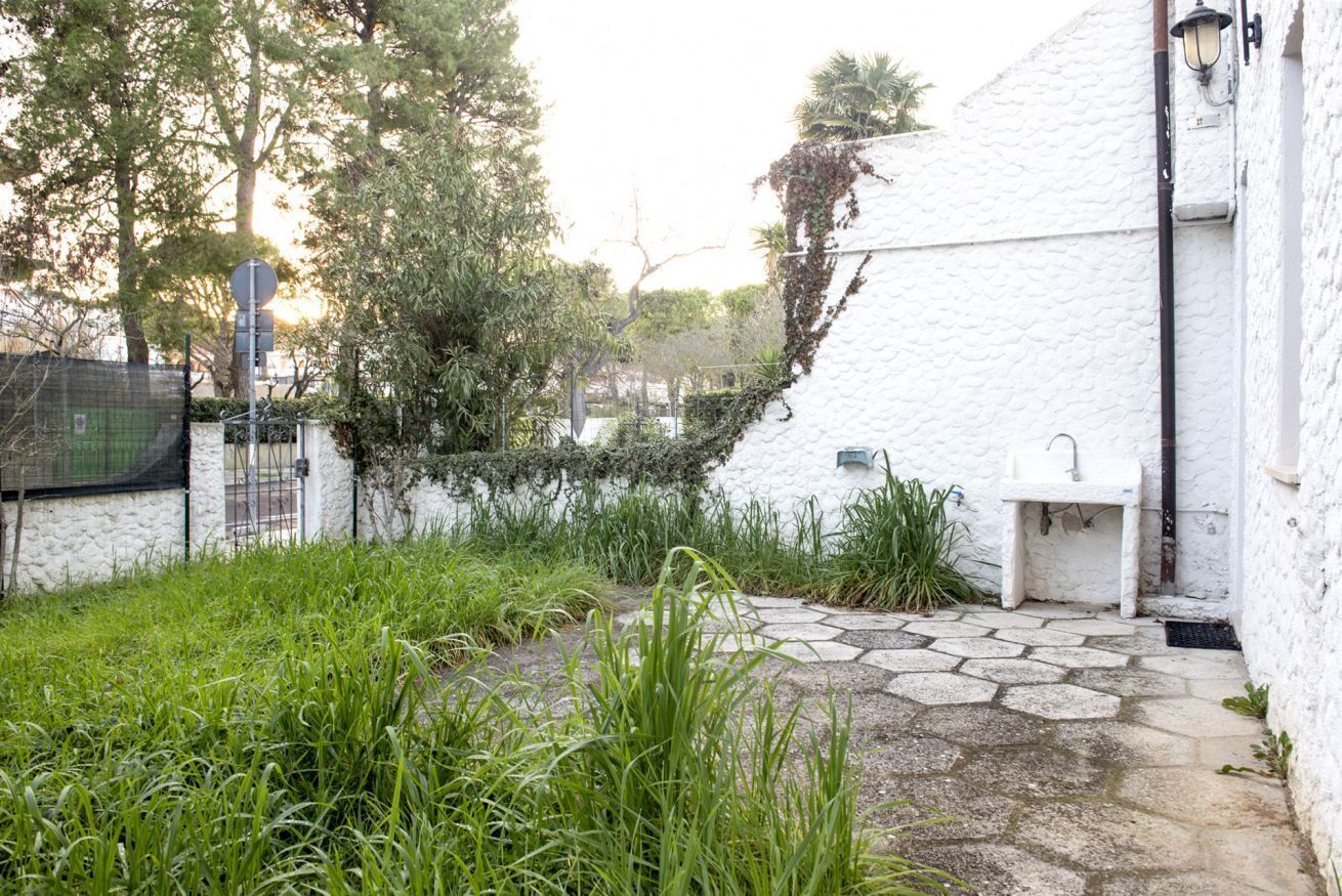 Un edificio bianco con un vialetto in pietra, un lavandino e del verde.