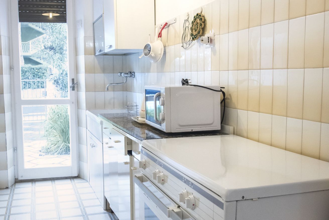 Cucina con mobili bianchi, forno a microonde e finestra vista su spazi verdi.