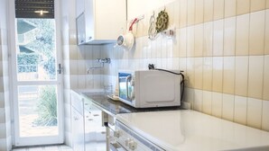 A kitchen with white cabinets, a microwave, and a window with a view of greenery. - M107 - Marcelli, three-room apartment with garden 200m from the sea (Marcelli)