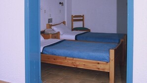 A room with two wooden beds, a small table, a chair, and a single hanging light fixture. - Friday Hotel (Hersonissos)