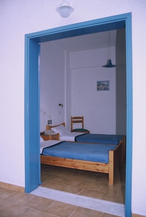 Ein Zimmer mit zwei Holzbetten, einem kleinen Tisch, einem Stuhl und einer einzelnen Pendelleuchte.