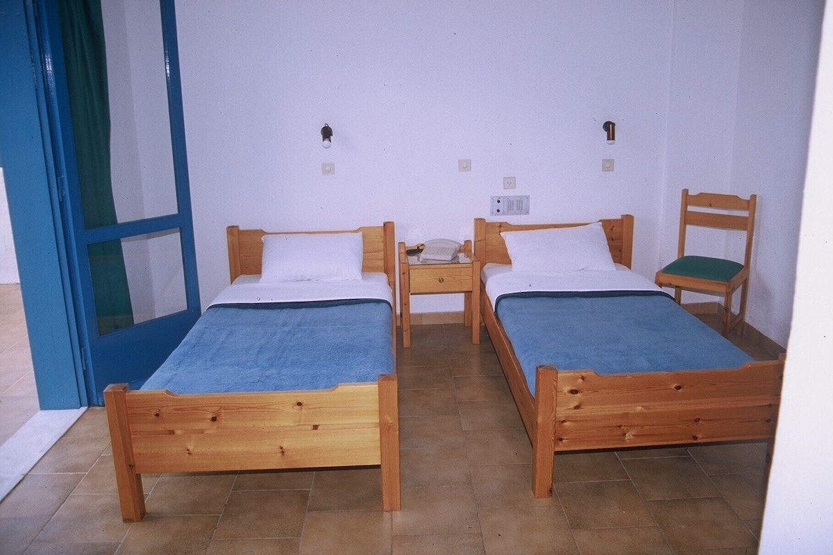 A room with two wooden beds, a chair, a small table, and a blue door.