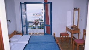 A room with two beds, a table with a flower vase, a chair, a desk with a mirror, and a view of the sea. - Friday Hotel (Hersonissos)
