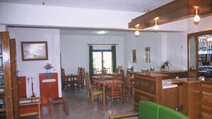 A room with wooden furniture, including a green sofa, wooden chairs, and a dining table. There are two small tables with red and blue patterns, and a mirror on the right wall. - Friday Hotel (Hersonissos)