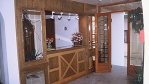A wooden reception desk with a glass partition, a small plant, and a door with a glass panel. - Friday Hotel (Hersonissos)