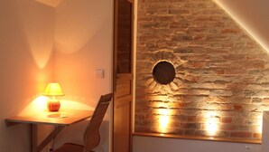Um quarto pequeno com teto inclinado, uma escrivaninha de madeira com abajur, uma cadeira e uma cama.