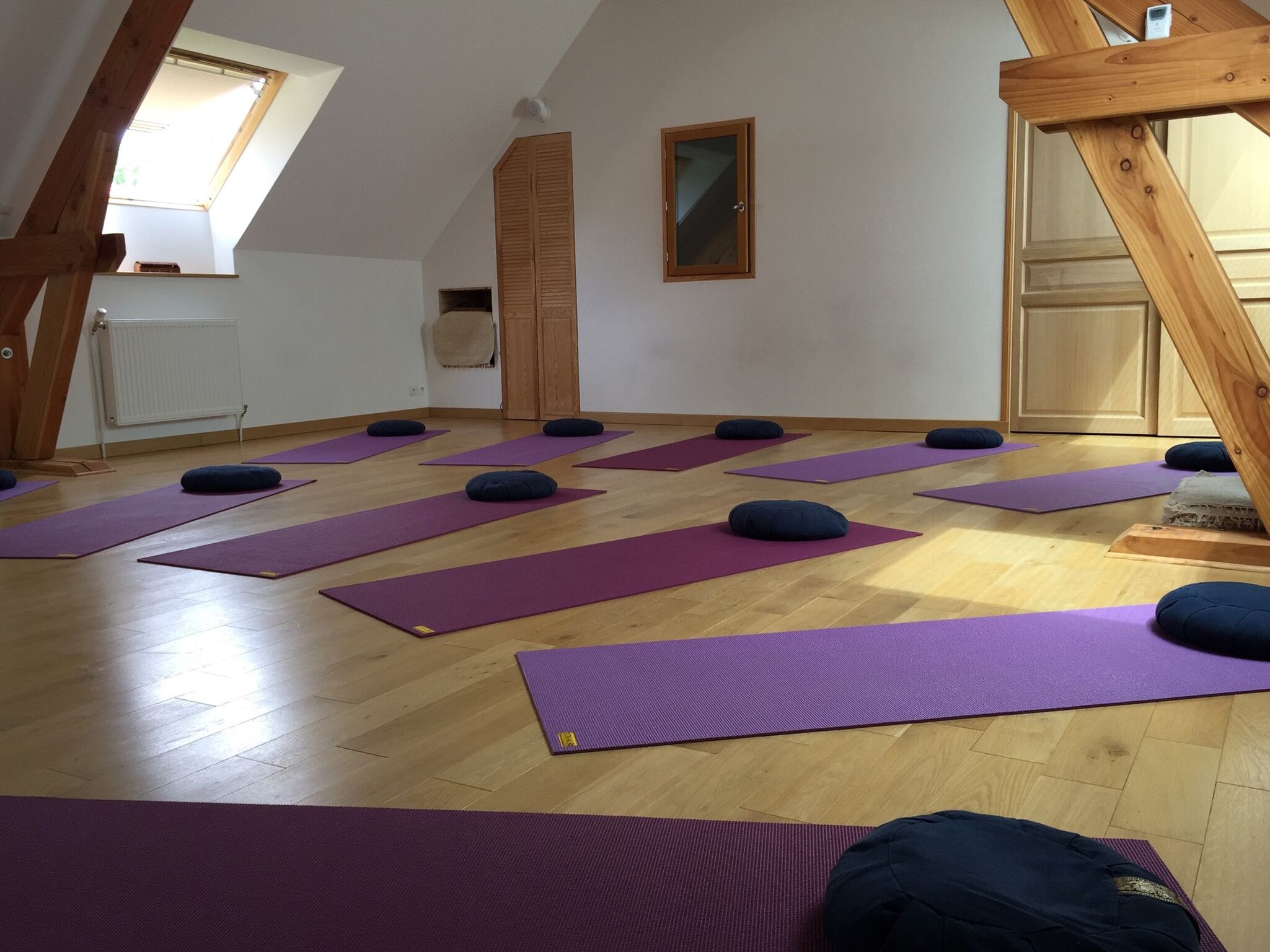 Un studio de yoga avec des poutres en bois, des tapis violets et des coussins noirs sur un plancher en bois.